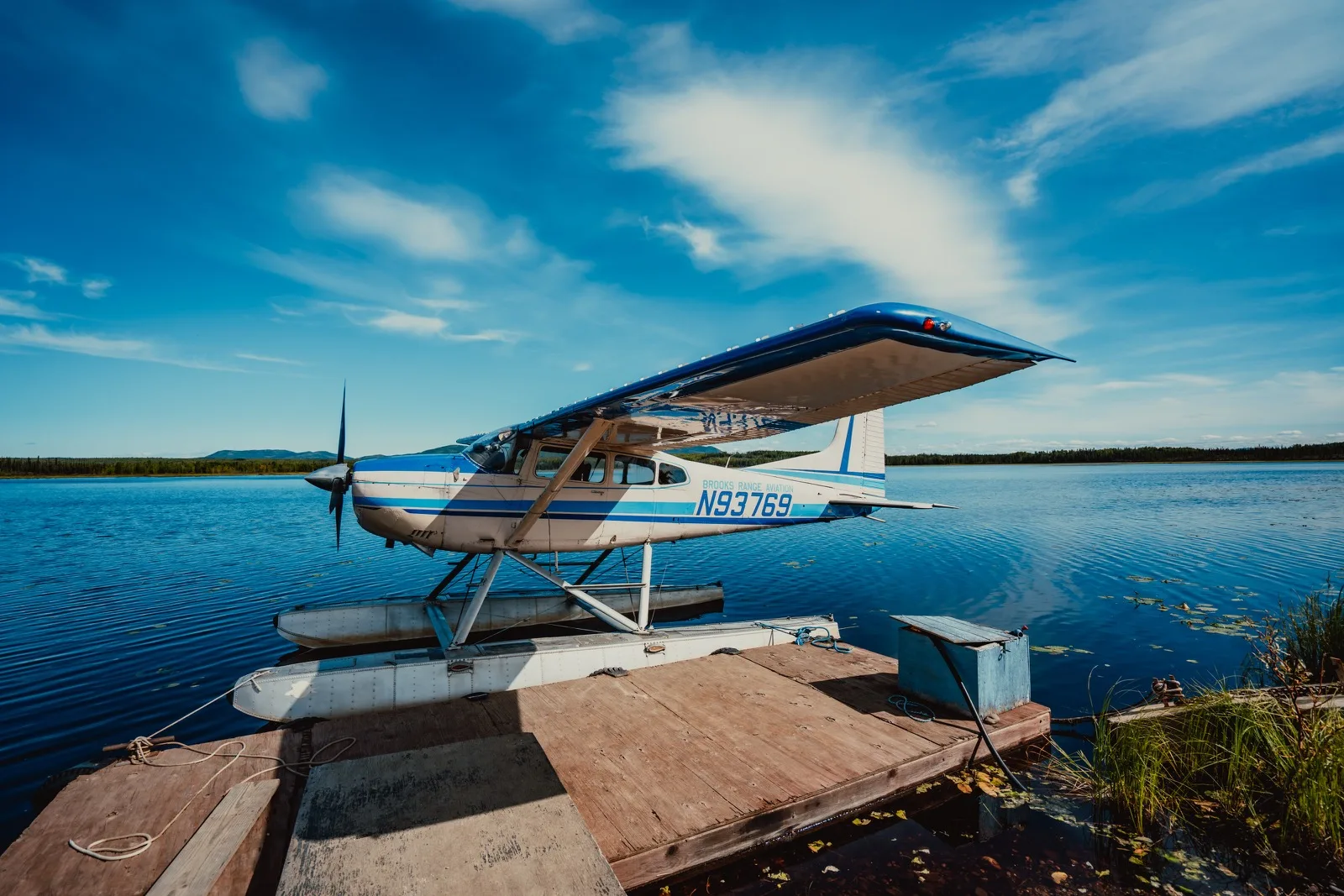 A blue floatplane tied beside a clear lake