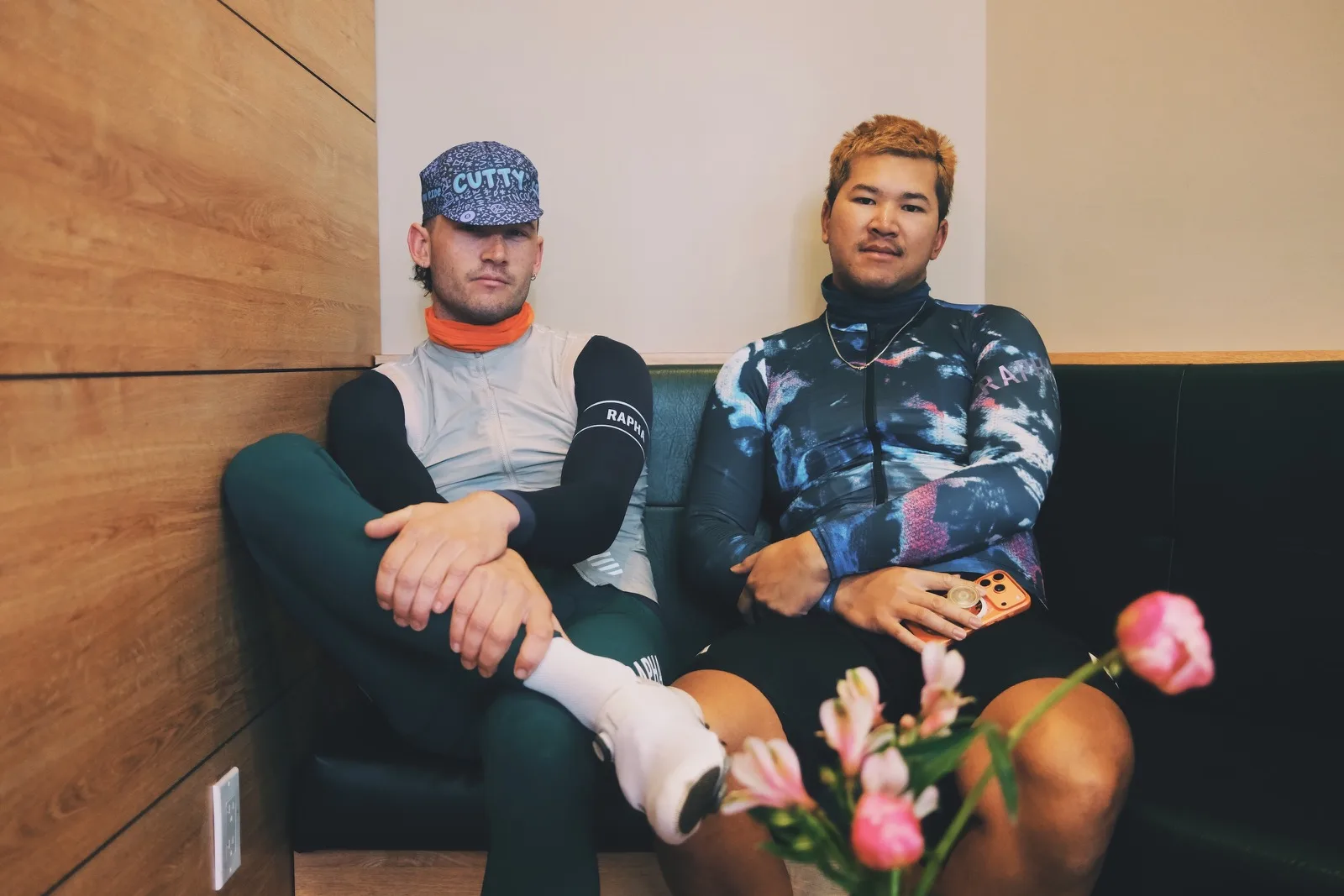 Two cyclists resting in a cafe with flowers in the foreground