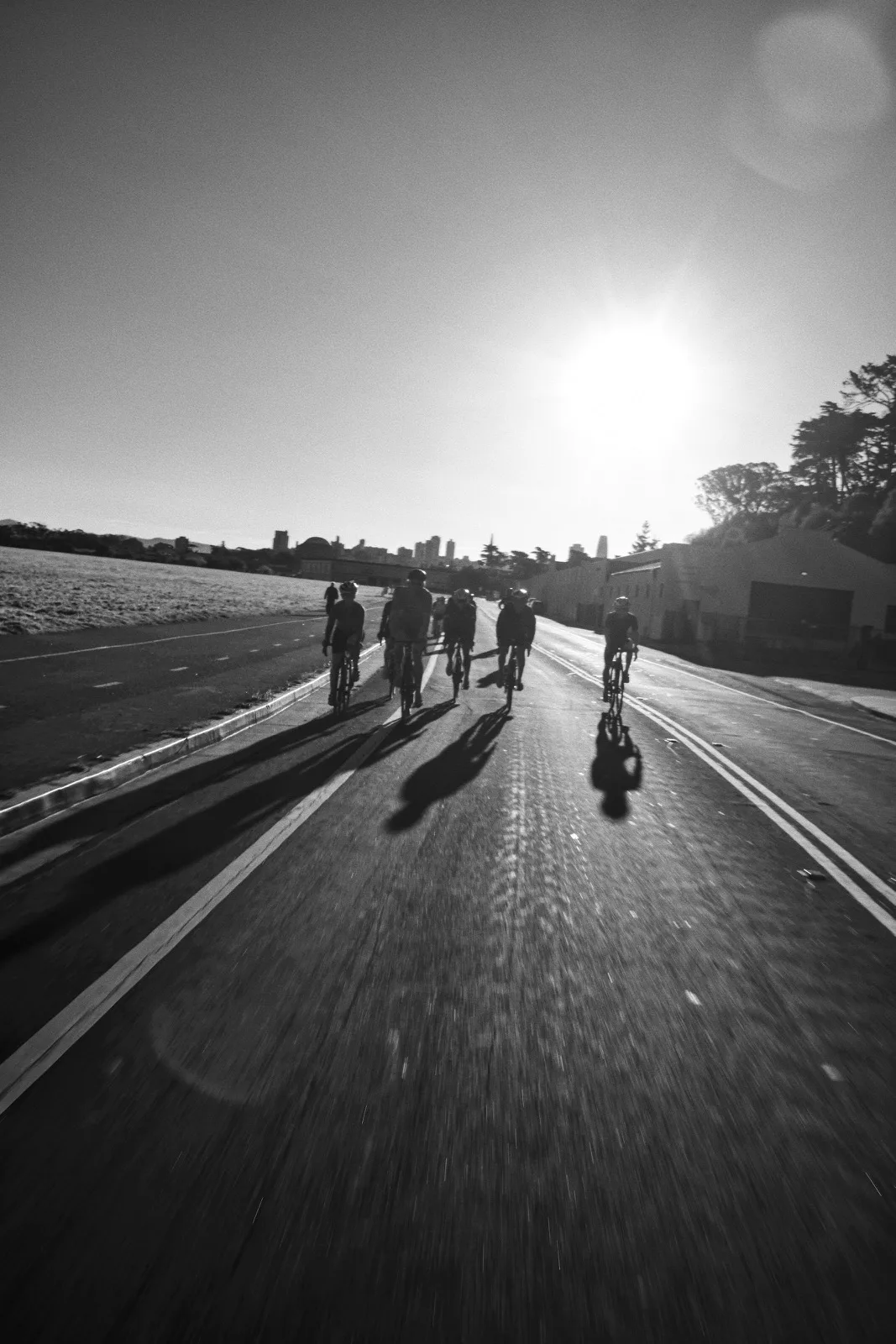 Cyclists and long shadows crossing a monochrome road