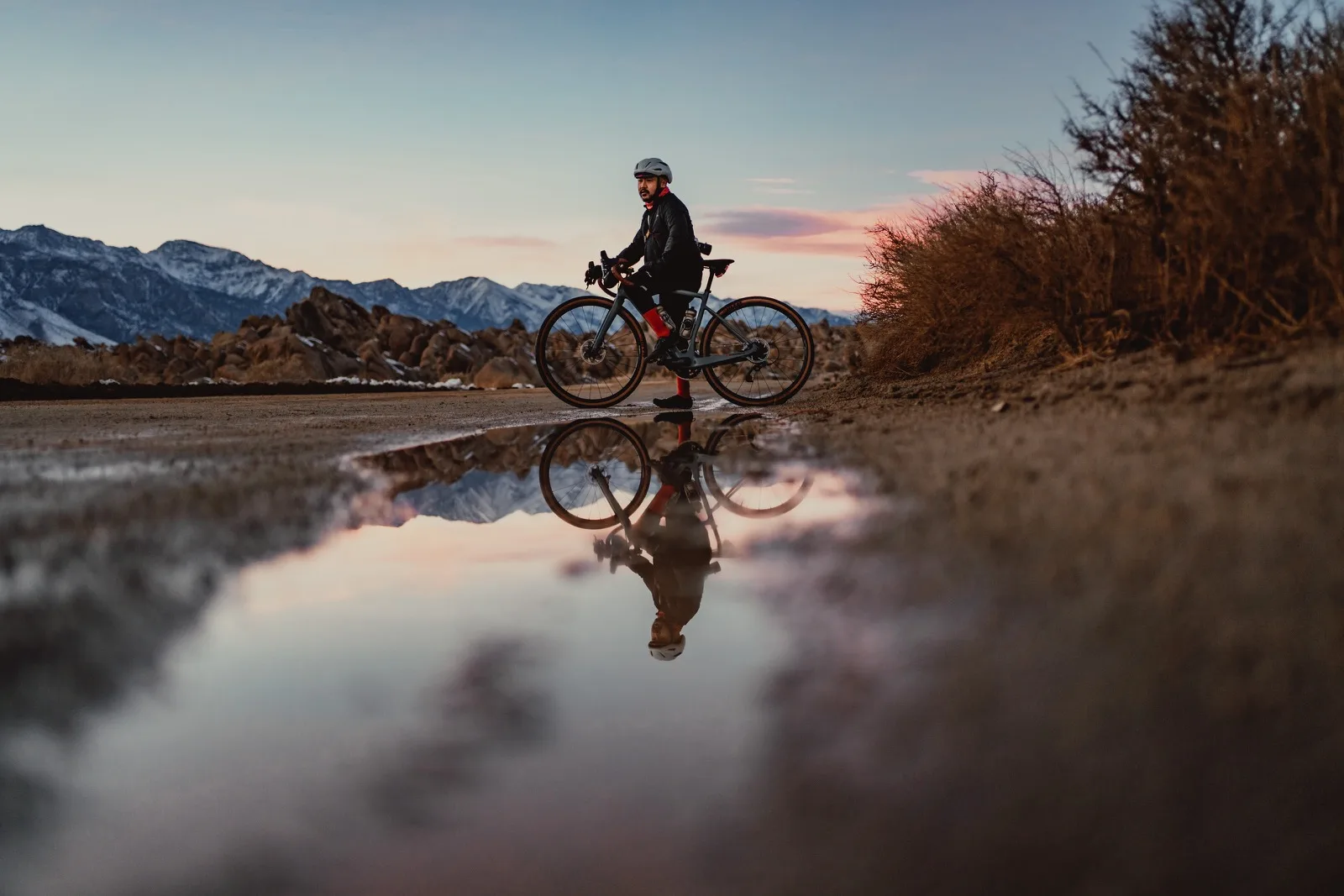 A cyclist and winter mountains reflected in a roadside pool