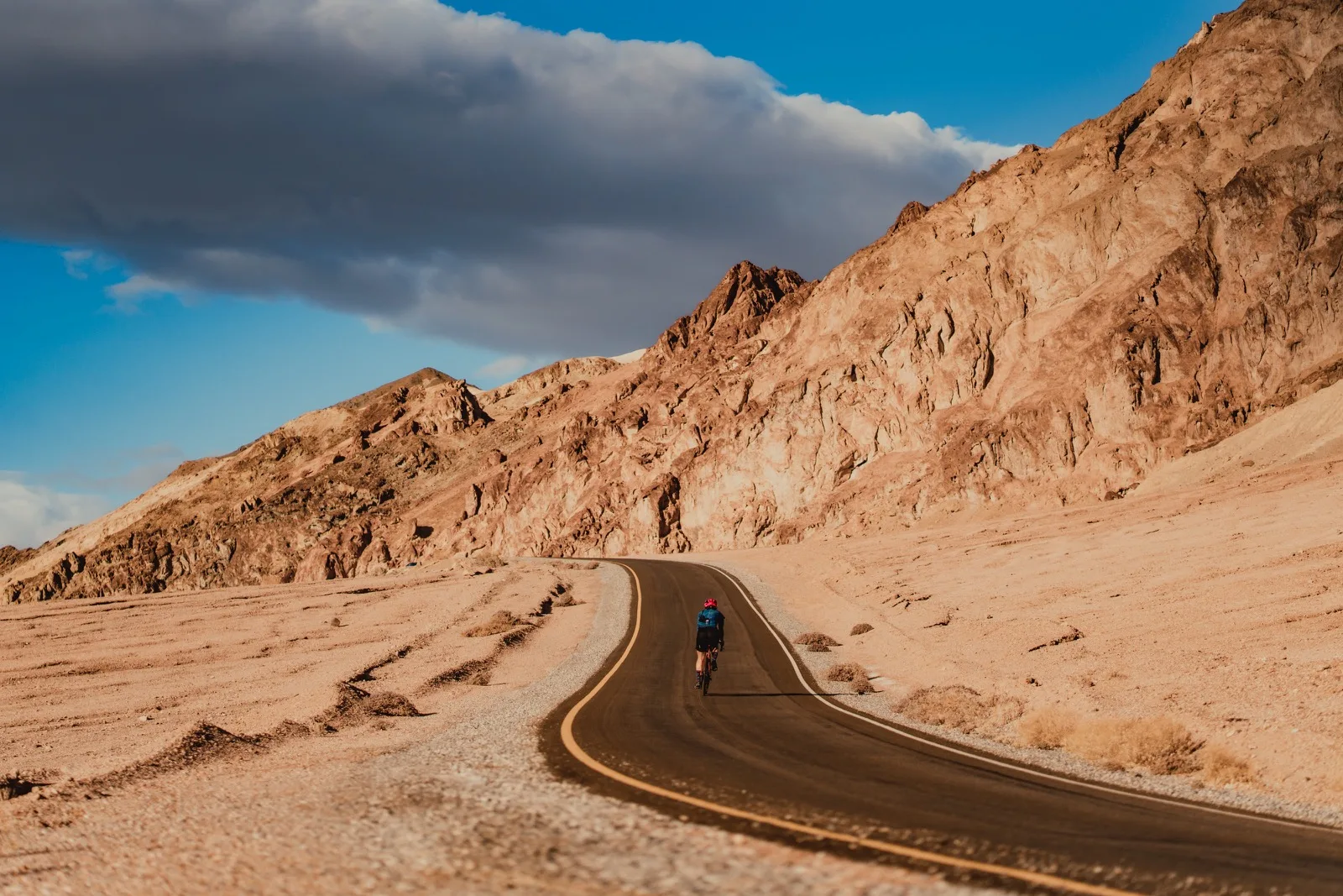 A tiny cyclist following a long ribbon of road through the desert