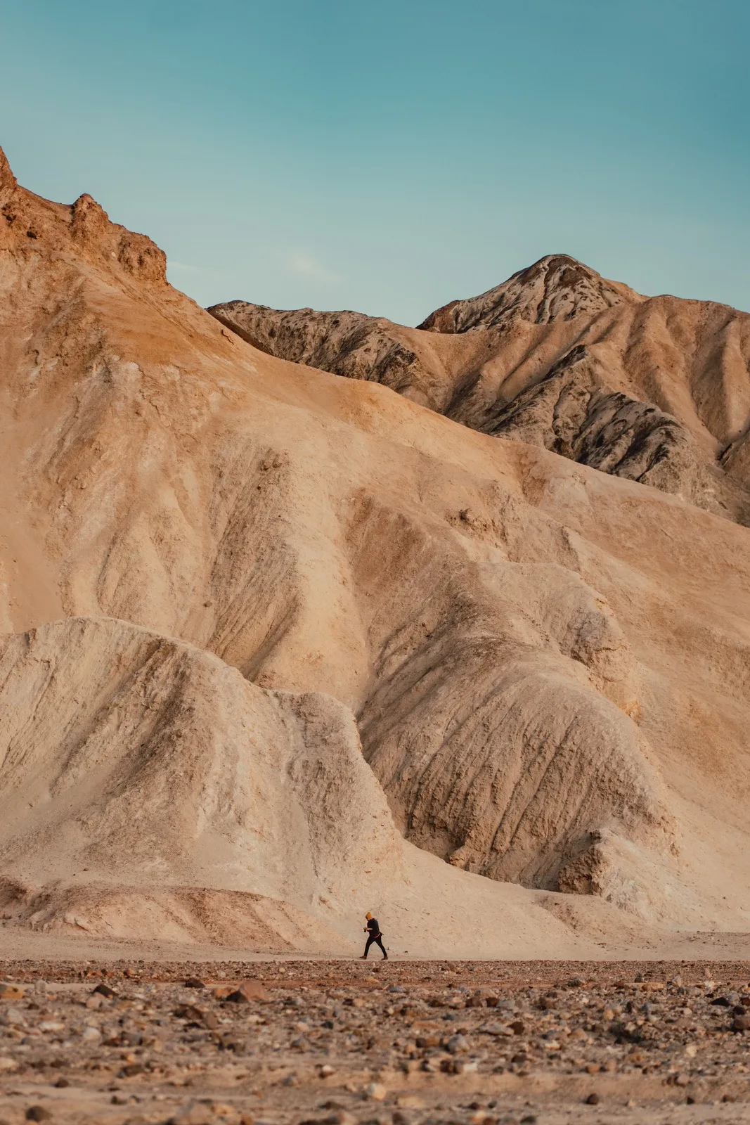 A lone figure walking below layered desert badlands