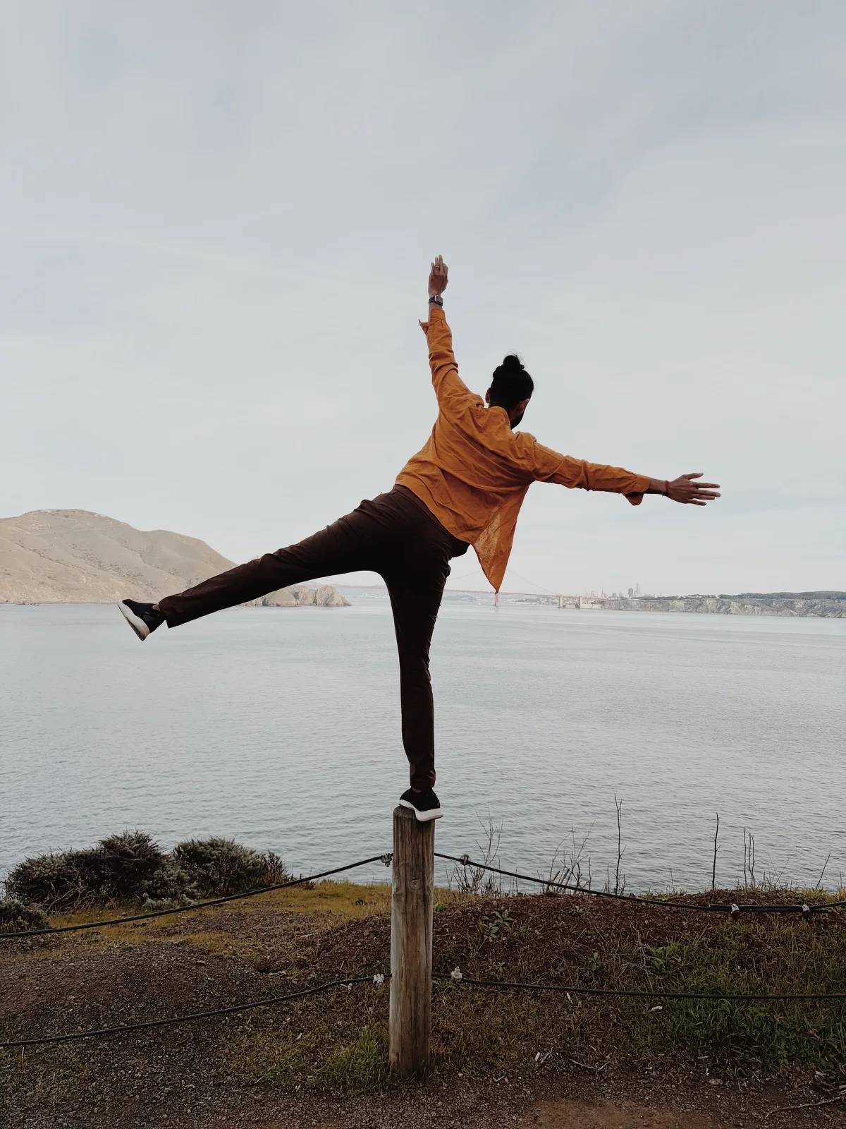 A person balancing playfully on one leg by the water