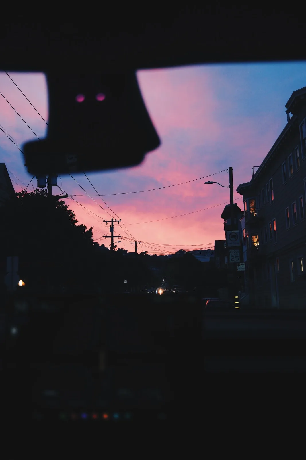 A blurred traffic signal against a pink neighborhood sky