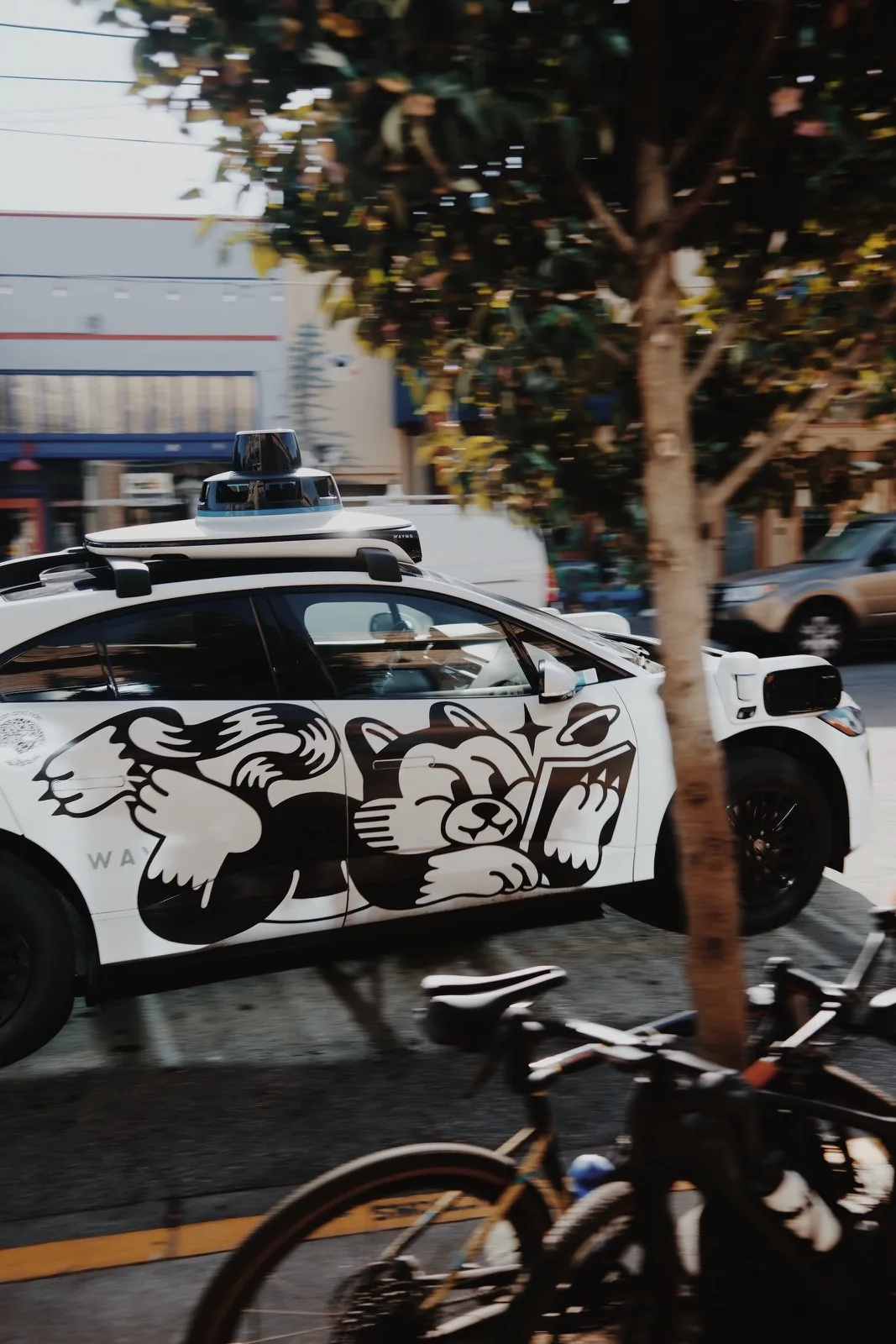 A Waymo car passing through a sunlit city intersection