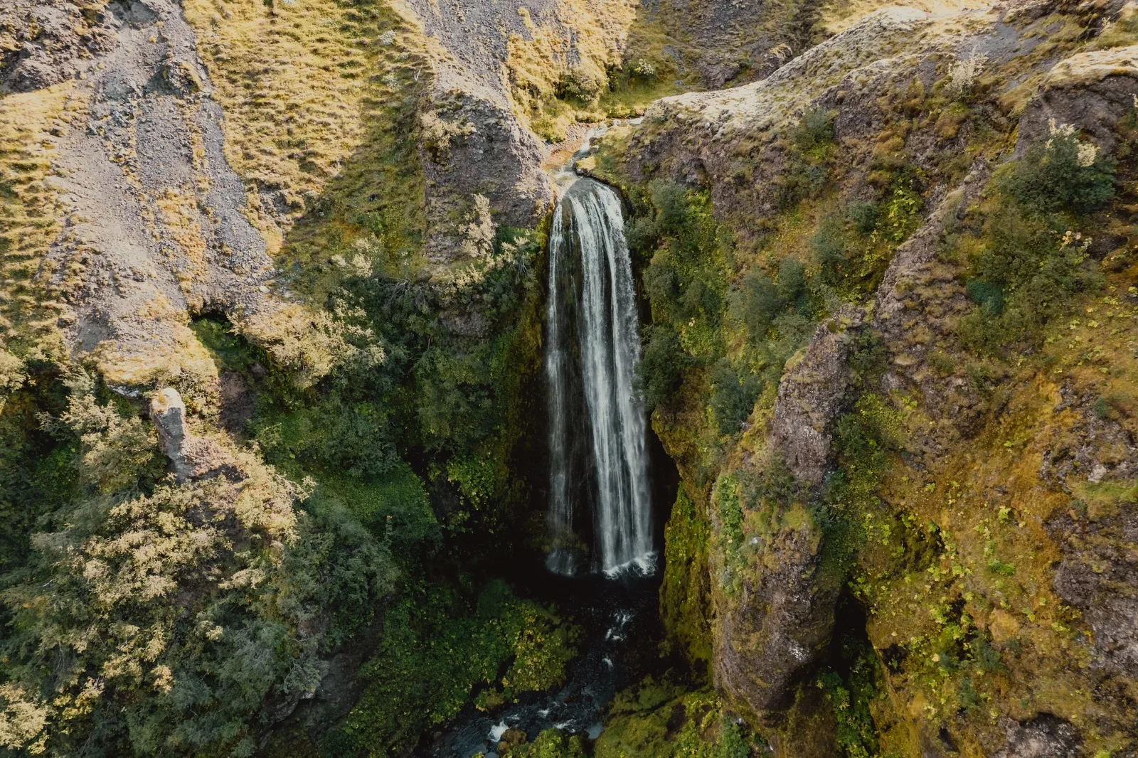 A waterfall dropping through a green canyon seen from above