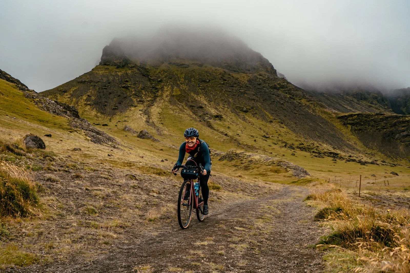 A cyclist descending beneath a cloud-covered green mountain