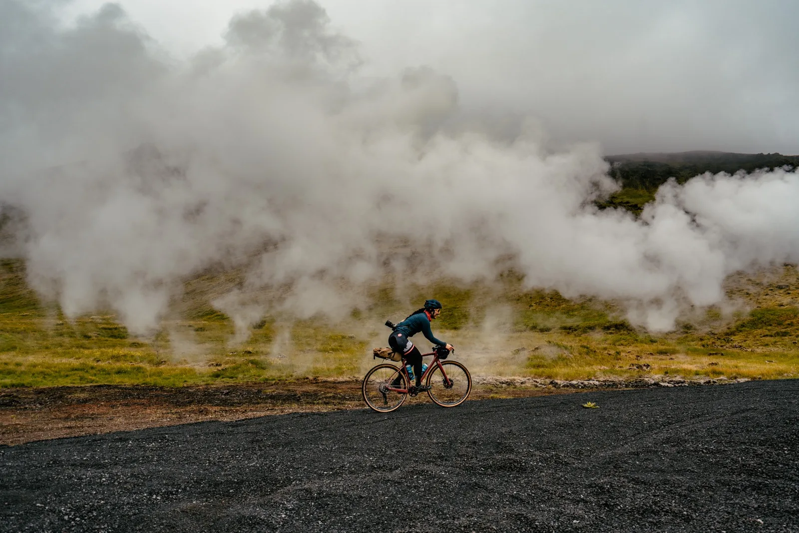 Cyclists passing a steaming geothermal hillside