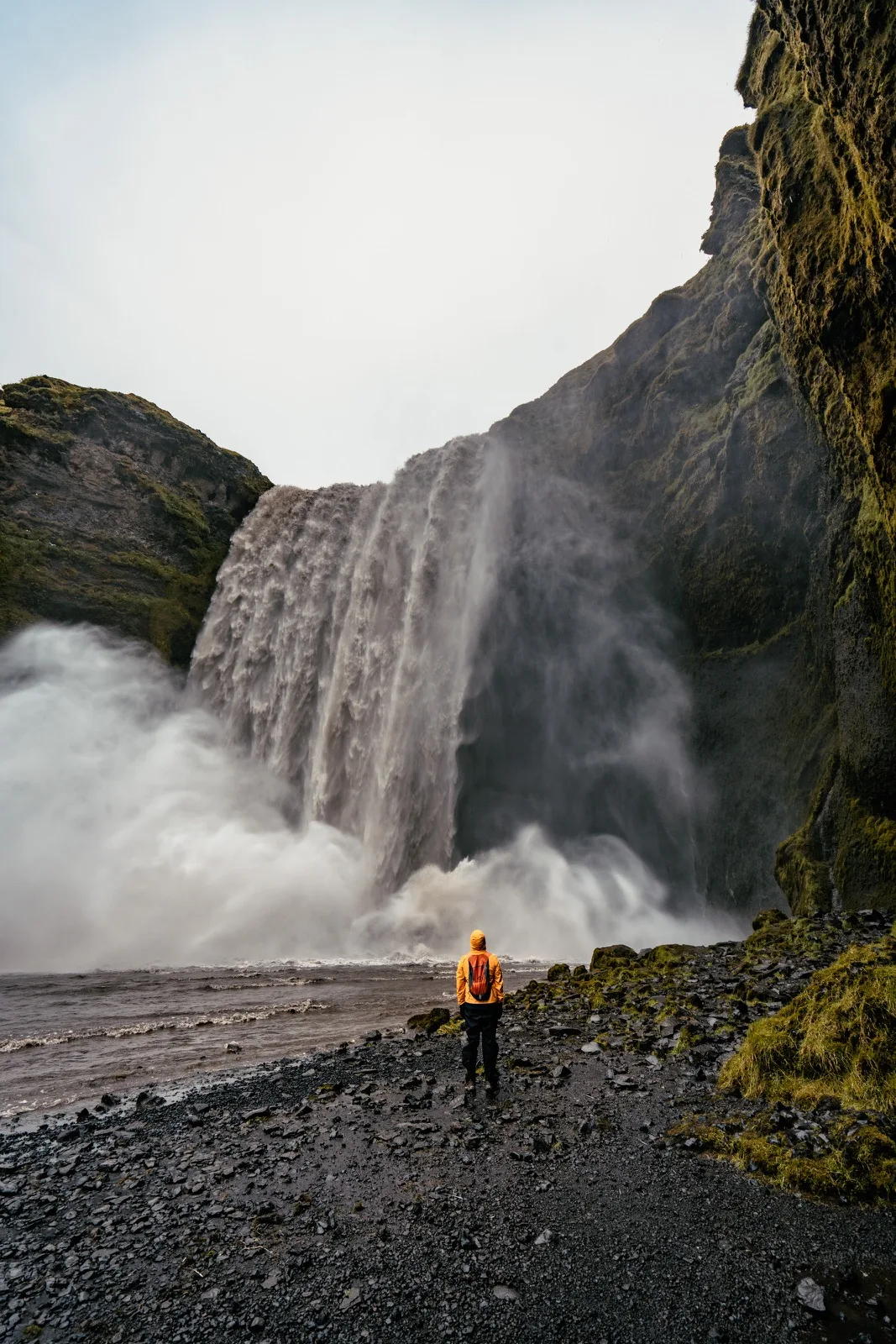 A tiny figure standing beneath a massive waterfall