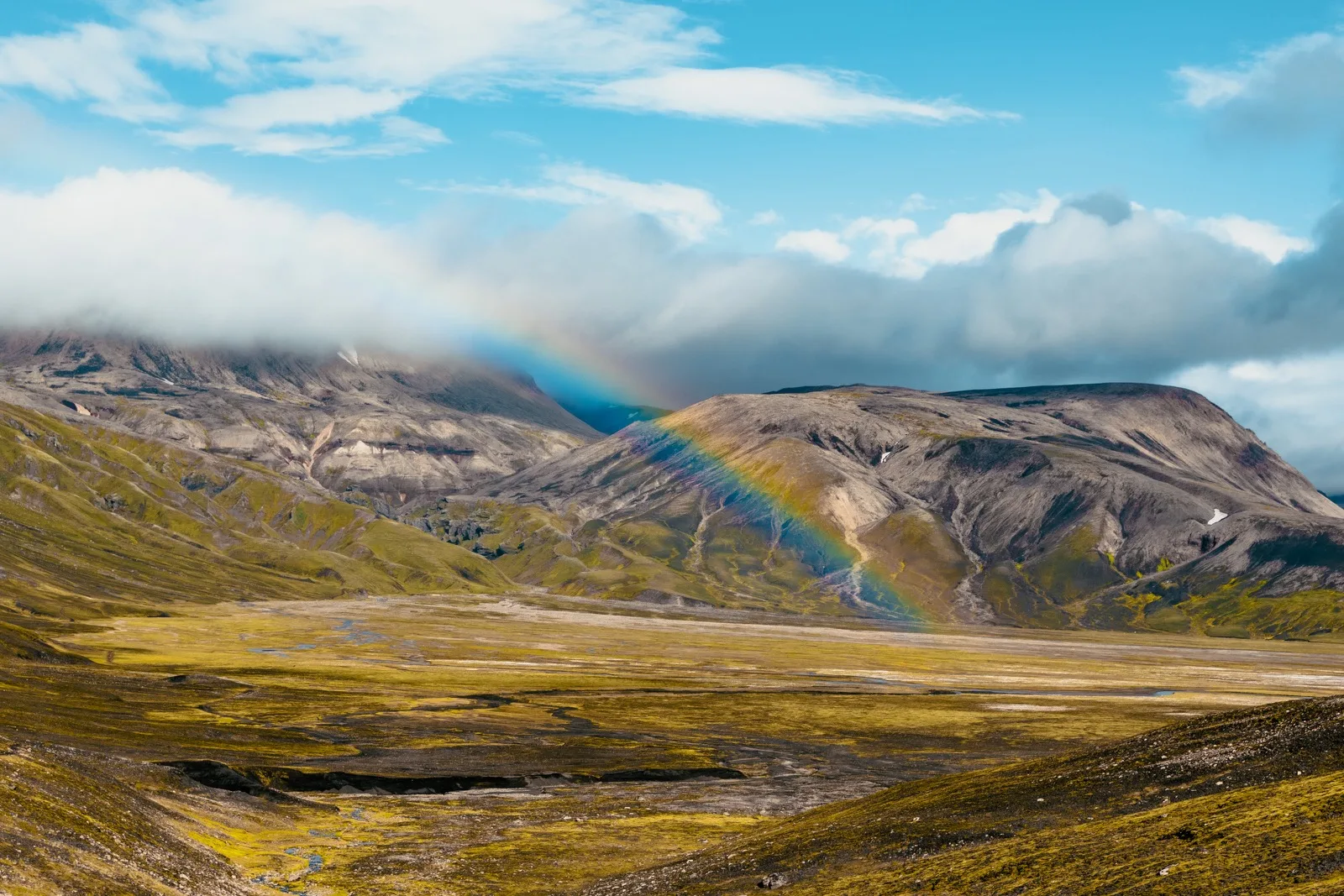 A rainbow crossing a broad green volcanic valley