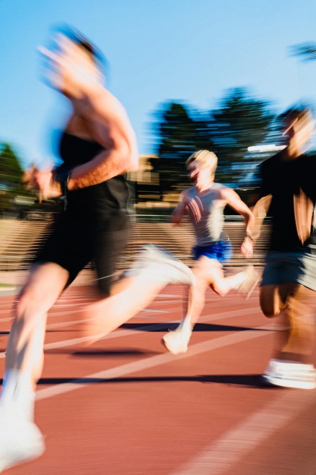 Motion-blurred runners crossing a sunlit track