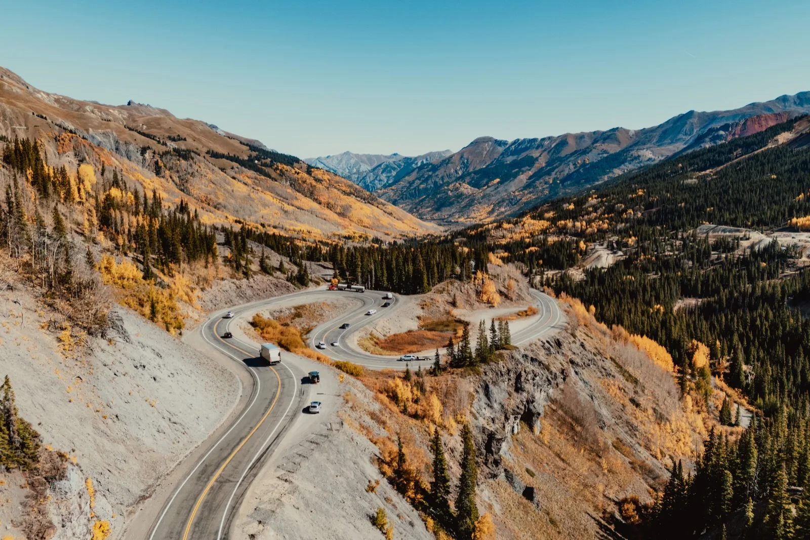 An aerial view of a winding road through an autumn mountain valley