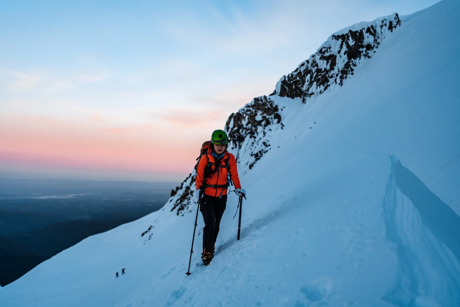 Climbers ascending a steep snow face above the valley