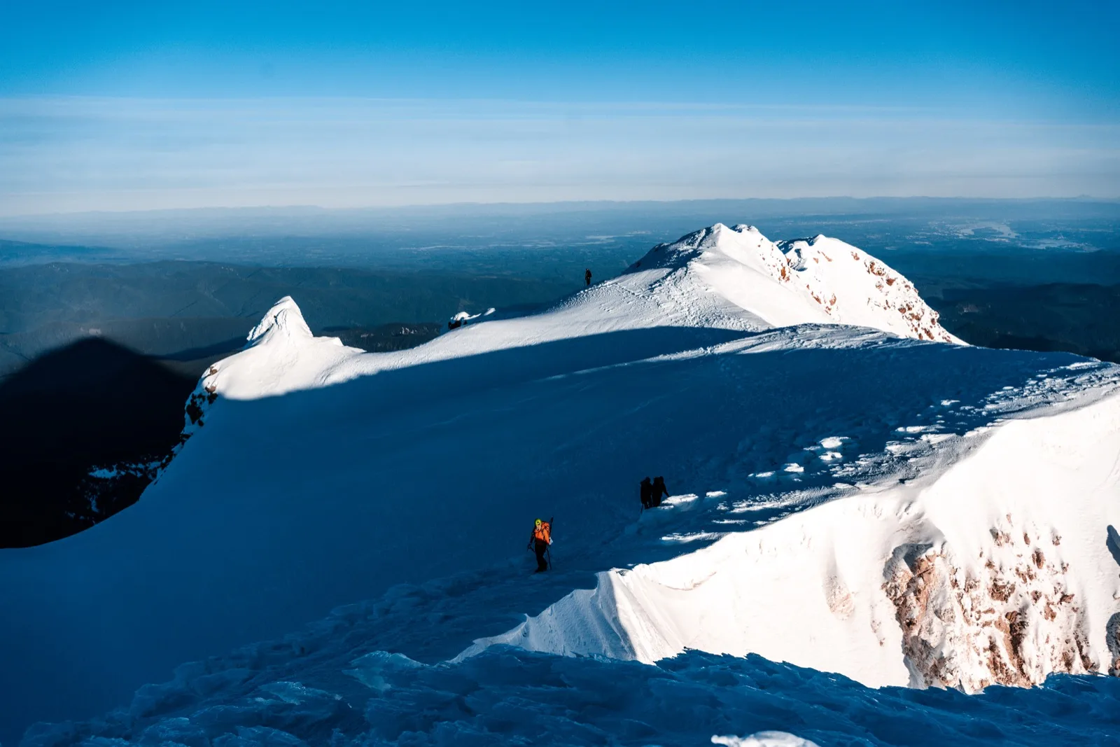 Tiny climbers tracing the edge of a broad snow ridge