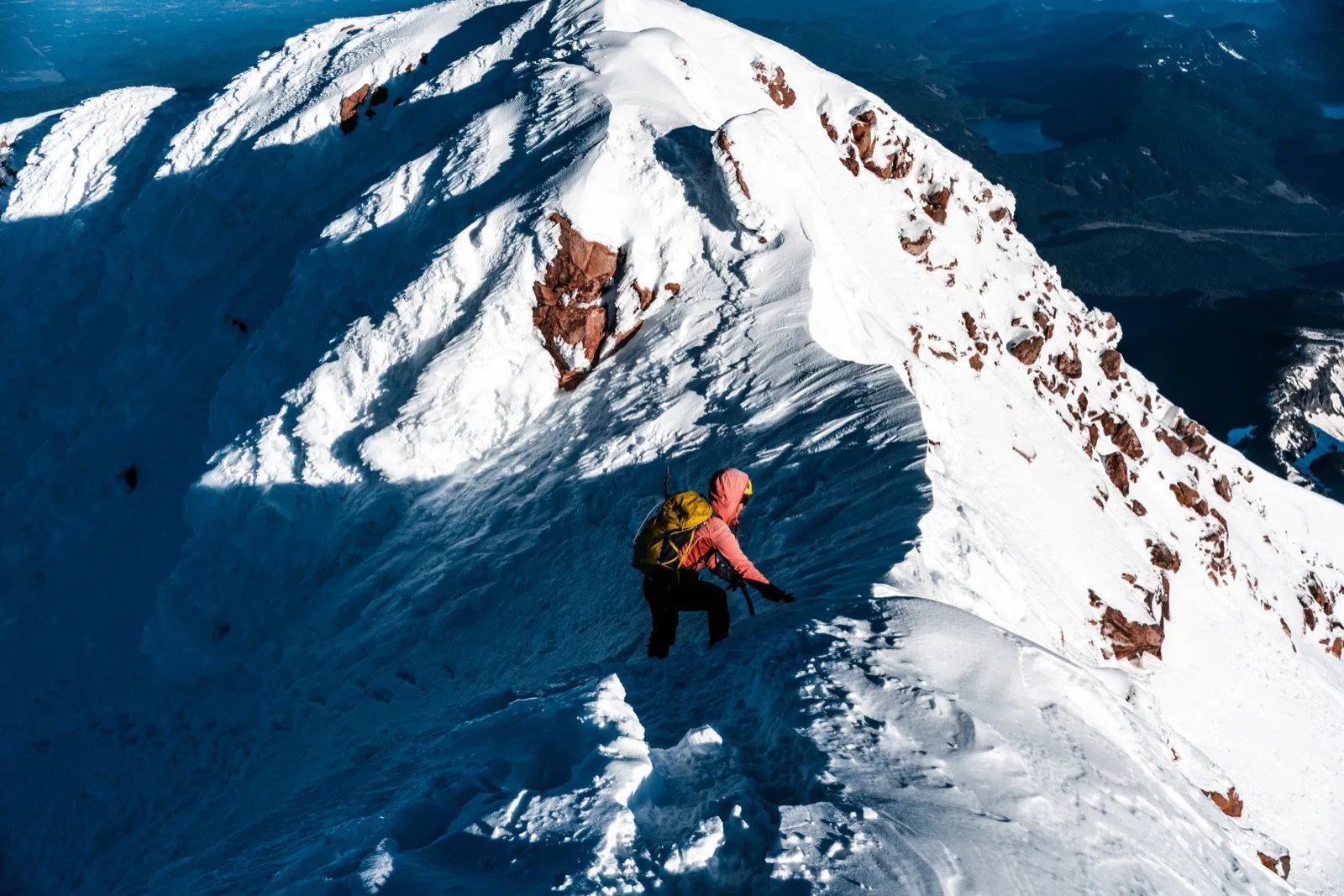 An orange-clad climber moving along a knife-edge ridge