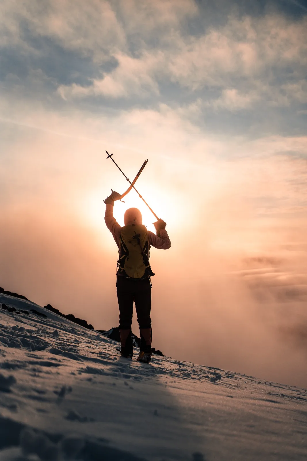 A climber celebrating in silhouette above the clouds